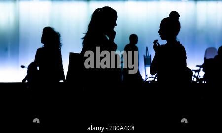 Silhouetten von zwei Teenager-Mädchen, die vor dem modernen Gebäude, in der Nacht, stehen und sprechen, und Menschen, die vorbeikommen, in hohem Kontrast schwarz und blau Stockfoto