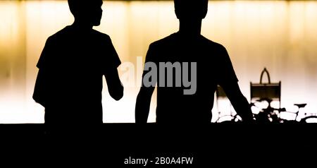 Silhouetten von zwei jungen Teenagern, die vor dem modernen Gebäude spazieren, in der Sommernacht in kontrastreichem Schwarz- und Orangenweiß Stockfoto