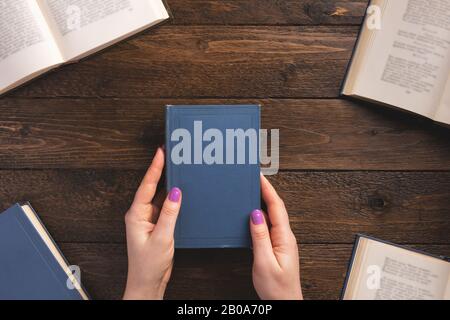 Weibliche Hände mit altem Buch. Bücher auf Holzhintergrund. Flaches Layout, Draufsicht, Kopierbereich. Stockfoto