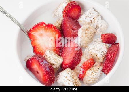 Zuckerbeschichtetes, geschreddertes Weizengetreide wird in einer Schüssel mit Milch und in Scheiben geschnittenen Erdbeeren serviert. Stockfoto