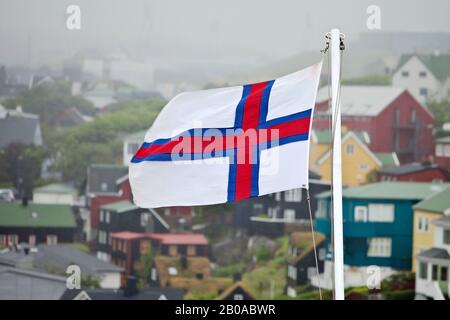 Flagge des Faeroeers vor Häusern in Nebel, auf den Färöern, in Streymoy, in Torshavn Stockfoto