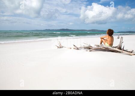 Mann mit lockigen Haaren, auf Holzschrammboden am weißen Sandstrand von Australien sitzend Stockfoto