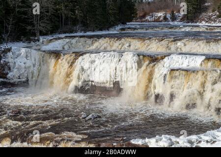 Lepreau Falls, New Brunswick, Kanada, im Winter. Die Stürze sind teilweise gefroren, goldenes Wasser fließt über den Rest. Stockfoto