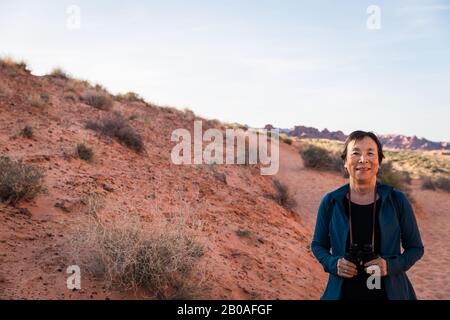Ältere asiatische Frau lächelt mit Fernglas in der Wüstenlandschaft Stockfoto