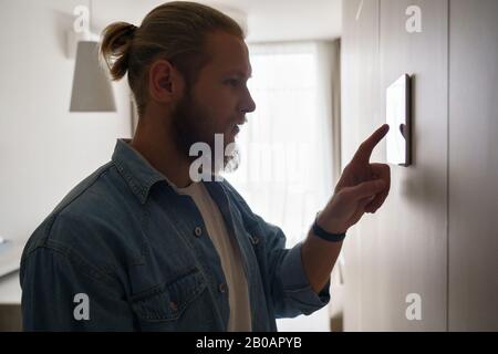 Junger Mann mit intelligentem Touchscreen-Gerät an der Wand Stockfoto