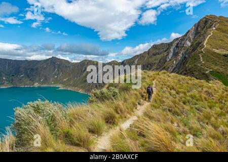 Junger männlicher Rucksacktourist, der auf dem magischen Quilotoa-Kratersee auf der Wanderung mit dem Namen Quilotoa-Schleife in der Anden-Gebirgskette bei Quito, Ecuador, spazieren geht. Stockfoto