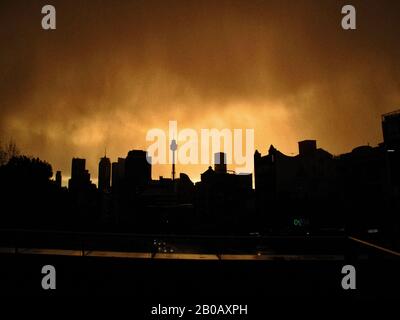 Dramatischer orangefarbener Himmel und Sturmlicht Über Sydney von William St Kings Cross mit einer Silhouette der Skyline der Stadt durch einen leichten Regenschleier Stockfoto