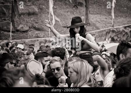 Eine junge Frau in einem Hut, einer Zigarette, einer Dose mit Bierfahrten auf A bemannt Schultern auf einer Tanzparty Mosh-Pit - Dokumentiert ein Musikfestival Sydney, Australien Stockfoto