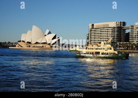 Sydney Opera House in sanftem Nachmittagslicht mit gelben und grünen Fähren, die sich unter blauem Himmel zum Circular Quay-Kai begeben Stockfoto