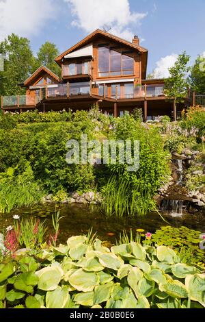 Rückseite aus goldbraun gebeiztem Stück sur Stück östlichen weißen Kiefer Holz und Holz Haus und schräg Garten mit Kaskadierung Wasserfall und Bach Stockfoto