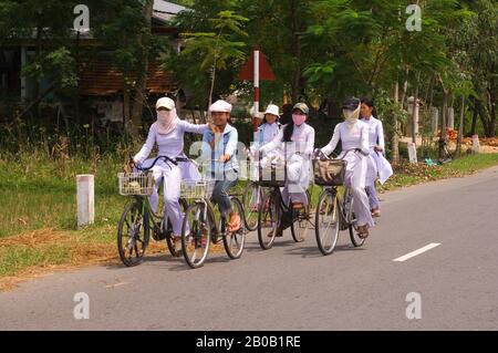 VIETNAM, IN DER NÄHE VON DA NANG, SCHULMÄDCHEN IM TRADITIONELLEN AO DAI (KLEID) AUF FAHRRÄDERN, DIE VON DER SCHULE KOMMEN Stockfoto