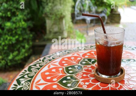 Ein halbes Glas Eiskaffee auf Dem Farbenfrohen Tisch im Patio Stockfoto