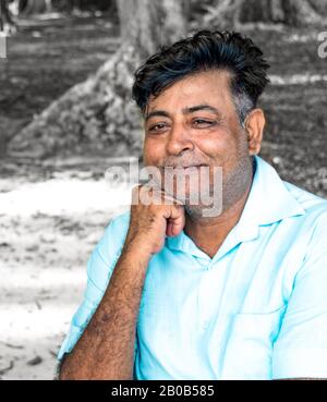 Fröhlicher und gesunder indianischer Mann mittleren Alters in seinen frühen 50er Jahren, posiert für Fotos mit lächelndem Gesicht, mit Hand am Kinn. Er ist im Ruhestand und lebt zufrieden. Stockfoto
