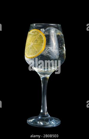 Transparenter Cocktail, erfrischendes Wasser in einem hohen Glas mit Eiswürfeln und einer runden Zitronenscheibe, Seitenansicht, isolierter schwarzer Hintergrund. Trinken Sie für den Stockfoto