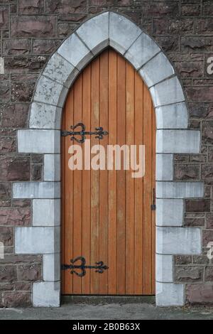 Eine alte, aus Holz gefertigte Domtür ist tagsüber in vertikaler Sicht von Stein auf einem Kirchengebäude in Europa umgeben. Stockfoto