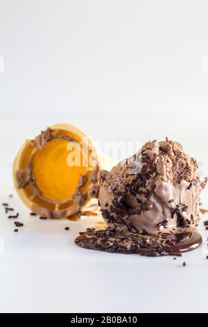 Gekrümmter Eiskegel mit Schokoladenicecream, Sauce und gesprinklert, isoliert auf weißem, selektivem vertikalem Bild Stockfoto