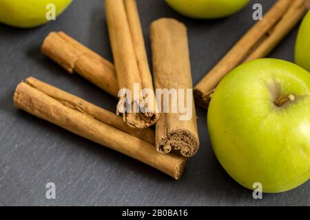 Zimtstangen und grüne Äpfel isoliert auf schwarzem Schieferhintergrund mit selektivem Fokus - Nahaufnahme horizontaler Bilder Stockfoto