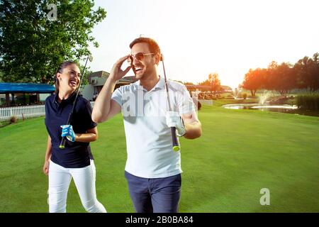 Glückliches Mädchen und gutaussehende Männer spielen während des Sonnenuntergangs Golf. Stockfoto