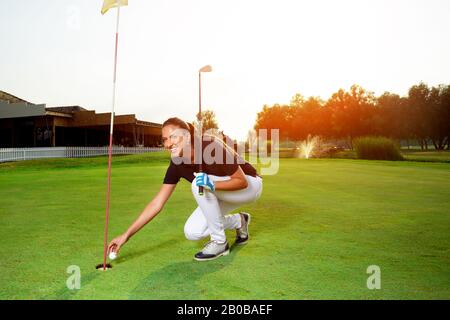 Ein weiblicher Golfer zieht ihre Kugel auf, die sich in der Nähe des Lochs befindet. Stockfoto