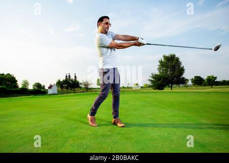 Ein gutaussehender Golfer übt sein Schwingen. Er macht sich bereit, den Ball zu schlagen. Stockfoto