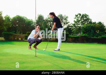 Ein schöner Golfer ist bereit, die Kugel zu schlagen, während ihr Golfpartner versucht, ihr etwas beizubringen. Stockfoto
