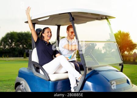 Glückliche Golfer fahren in einer Golfkarre. Stockfoto