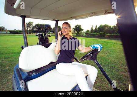 Ein weiblicher Golfer spricht am Telefon, während er in einer Golfkarre sitzt. Stockfoto