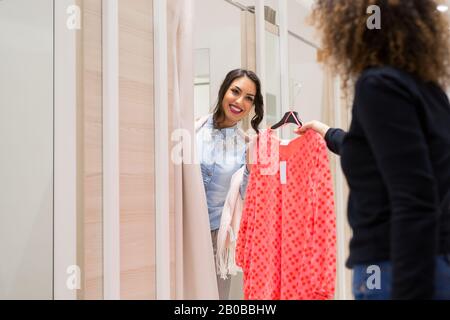 Zwei Arbeitskollegen übergeben sich gegenseitig Kleidung, um sich zu versuchen. Stockfoto