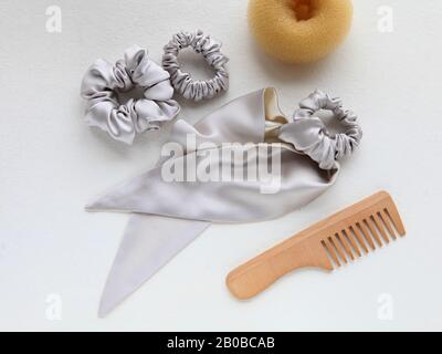 Haarbürste aus Holz, Barrette und Seide Scrunchy isoliert auf weiß. Flat Lay Frisierwerkzeuge und Accessoires Color Hair Scrunchies, Elastisches Haar Stockfoto