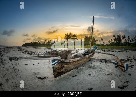 Traditionelles Holzboot bei Sonnenuntergang am tropischen Strand mit Palmen und weißem Sand am Strand von Diani, Watamu Kenia und Sansibar, Tansania Stockfoto