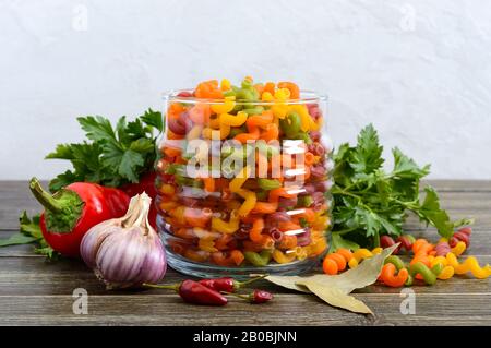 Cavatappi färbte rohe Pasta in einem Glasbecher, frisches Gemüse, Grüns auf einem Holzhintergrund. Nudelkolorata. Pasta mit Gemüse. Ellenbogenmakaroni Stockfoto