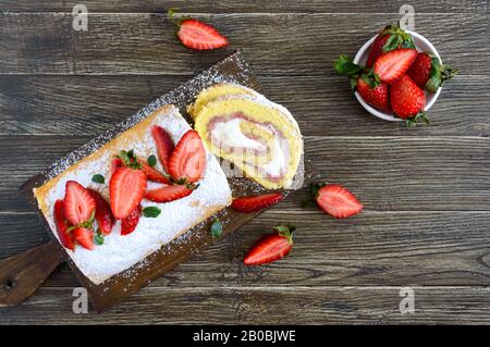 Süße Keksrolle mit Erdbeeren und Sahne auf Holzgrund. Draufsicht. Stockfoto