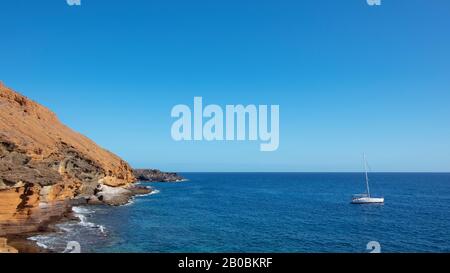 Gemütliche, abgeschiedene Bucht mit einer schwimmenden Yacht in der Nähe des farbenprächtigen, erodierten Vulkankegels, bekannt als Montana Amarilla, Costa del Silencio, Tenera, Spanien Stockfoto