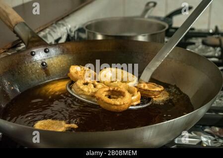 Ein Küchenchef Frites Indisch Pakora Zwiebel klingelt in heißem Öl über einem Gasherd in einer Restaurantküche Stockfoto