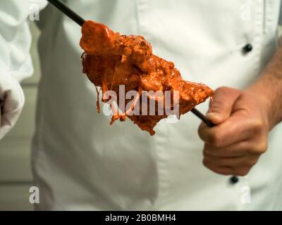 Ein indischer Koch schiebt mariniertes Huhn auf einen langen Metallküchespieß, der für eine Tandoori-Küche bereit ist. Stockfoto