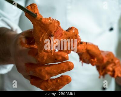 Ein indischer Koch schiebt mariniertes Huhn auf einen langen Metallküchespieß, der für eine Tandoori-Küche bereit ist. Stockfoto