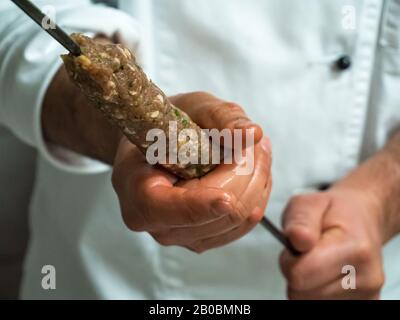 Ein indischer Koch schiebt mariniertes Lamm auf einen langen Metallküchespieß, der für eine Tandoori-Küche bereit ist. Stockfoto