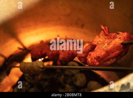 Nahaufnahme der Marinierten Hühnerkocht in einem offenen Tandoori-Inder-Ofen. Der heiße Ofen kocht das orangefarbene Fleisch langsam. Stockfoto