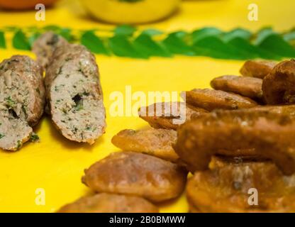 Nahaufnahme von indischen, tiefgebratenen Zwiebelringen und Lammkebab mit Minze und Kräuterkutney auf einem leuchtend gelben Hackbrett. Stockfoto