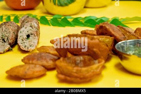 Nahaufnahme von indischen, tiefgebratenen Zwiebelringen und Lammkebab mit Minze und Kräuterkutney auf einem leuchtend gelben Hackbrett. Stockfoto