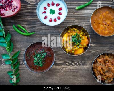 Blick auf einige authentische, frisch gekochte indische Thali Curries auf einer rustikalen Holzoberfläche. Stockfoto