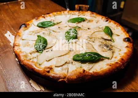 Köstliche Pizza mit gehackten Birnen und Dor Blaukäse liegt auf einem Holztisch. Stockfoto
