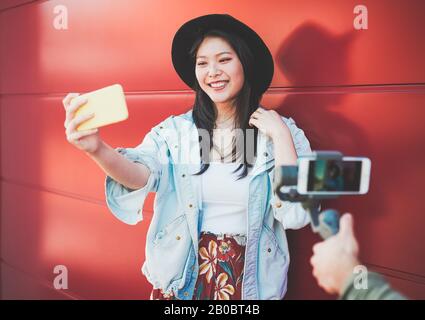 Trendige asiatische Frau schwungvoll, während sie Smartphone im Freien benutzt - Glückliches chinesisches Mädchen, das mit neuer Trendtechnologie Spaß hat - Mode, soziales Netzwerk, Technik Stockfoto