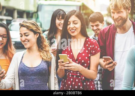 Fröhliche tausendjährige Freunde, die Smartphones am Busbahnhof nutzen - Junge Studenten, die nach der Schule im Freien Spaß haben - Freundschaft und Stadtlif Stockfoto