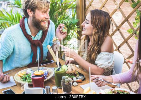 Junge Paare essen Brunch und trinken Smoothie-Schüssel in der Vintage-Bar - Fröhliche Leute, die ein gesundes Mittagessen haben und im trendigen Restaurant plaudern - Essen TR Stockfoto