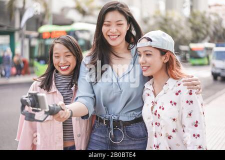 Fröhliche asiatische Mädchen machen Vlog-Video am Busbahnhof - Trendige Freunde Blogging für soziale Medien im Freien - Technologie Lifestyle-Trends, Stadt, lässige Clot Stockfoto