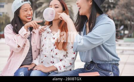 Trendige asiatische Mädchen, die im Freien zusammen Spaß haben - Junge Frauen, die mit Blasengummi spielen - Trends, Jugend, Jahrtausende Generation und Freundschaftskontra Stockfoto