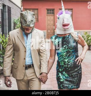 Verrücktes Senioren-Paar mit T-rex und Hähnchenmaske durch die Stadtstraße spazieren - Alte Trend-Leute, die zusammen Spaß haben - Absurdes und lustiges Trend-Konzept Stockfoto