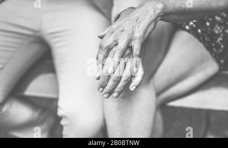 Die Hände zeigen, dass ein älteres Paar zärtliche Momente im Freien hat - Reife Leute draußen auf einer Bank sitzen - aktive Lebensfreude bei Liebe, Alter und fröhlichen Senioren Stockfoto