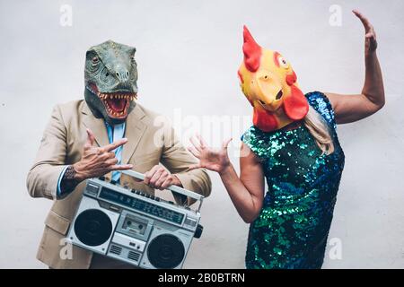 Verrücktes Senioren-Paar tanzt für die Silvesterparty mit t-rex und Hähnchenmaske - Alte Trend-Leute, die Spaß beim Musikhören mit Boombox-Stereo haben Stockfoto